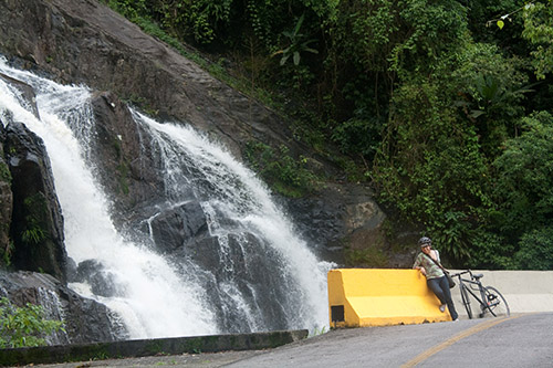 Sarinha com sua fixa em frente à uma cachoeira à beira da estrada de manutenção do Complexo Ecovias