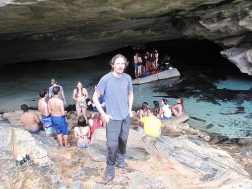 Lex vestido de espeleólogo na entrada de uma caverna cheia de turistas com traje de banho no lago